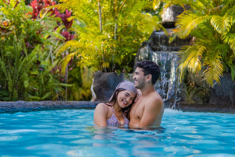 People enjoying a romantic moment in a tropical swimming pool with a waterfall backdrop.