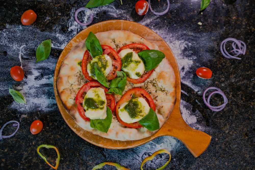 Rustic pizzas topped with fresh herbs and vegetables on a dark stone surface.