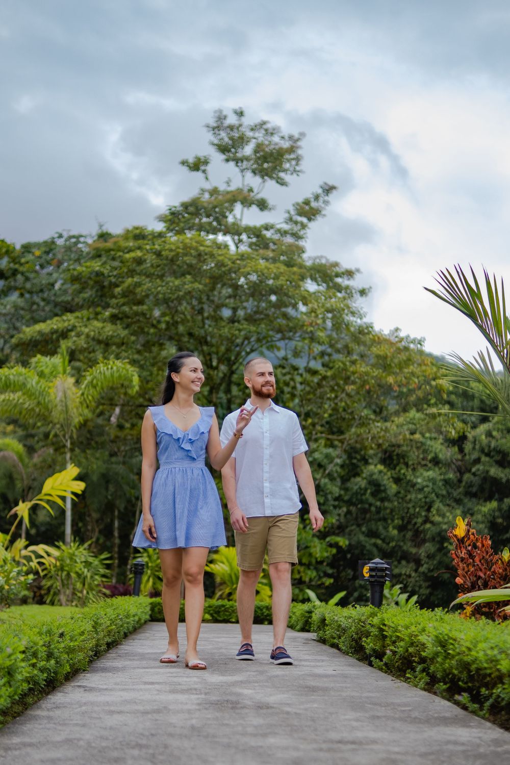 A couple walking on a garden pathway surrounded by lush tropical landscaping and palm trees.