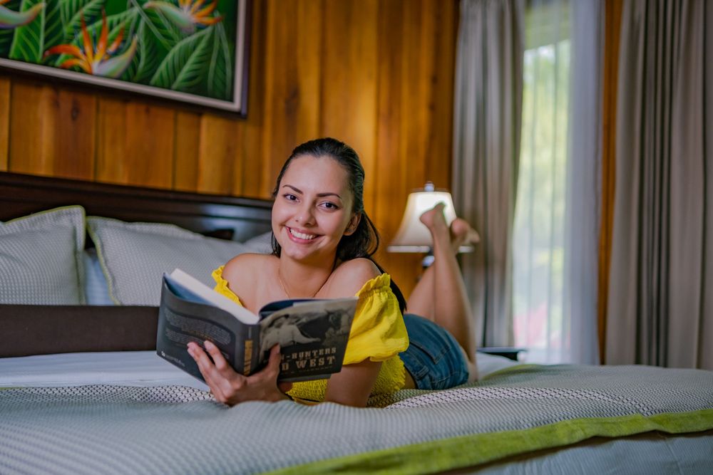 A person relaxing on a bed while reading a book in a cozy bedroom with wooden walls.