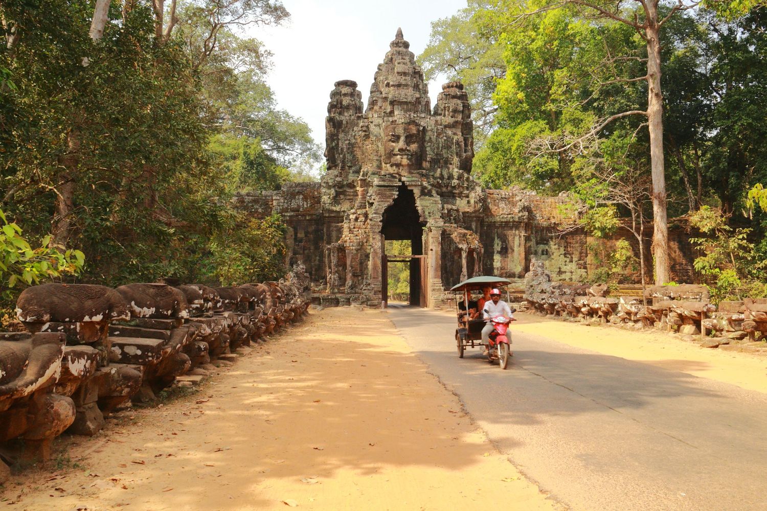 Stone gateway entrance to Angkor temple complex with path leading to ornate towers.