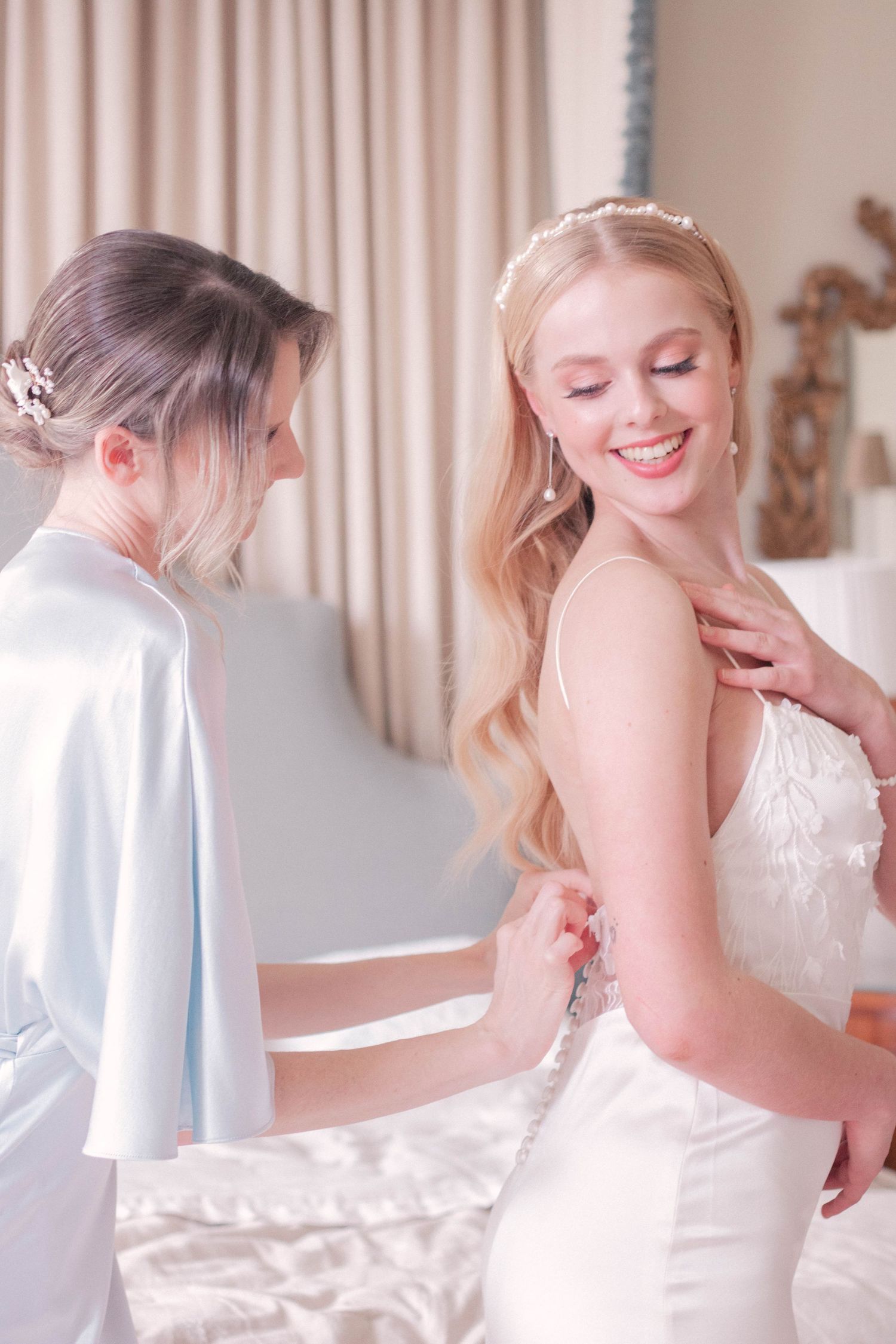 Bride in white lace dress smiling while getting final adjustments to her wedding gown.