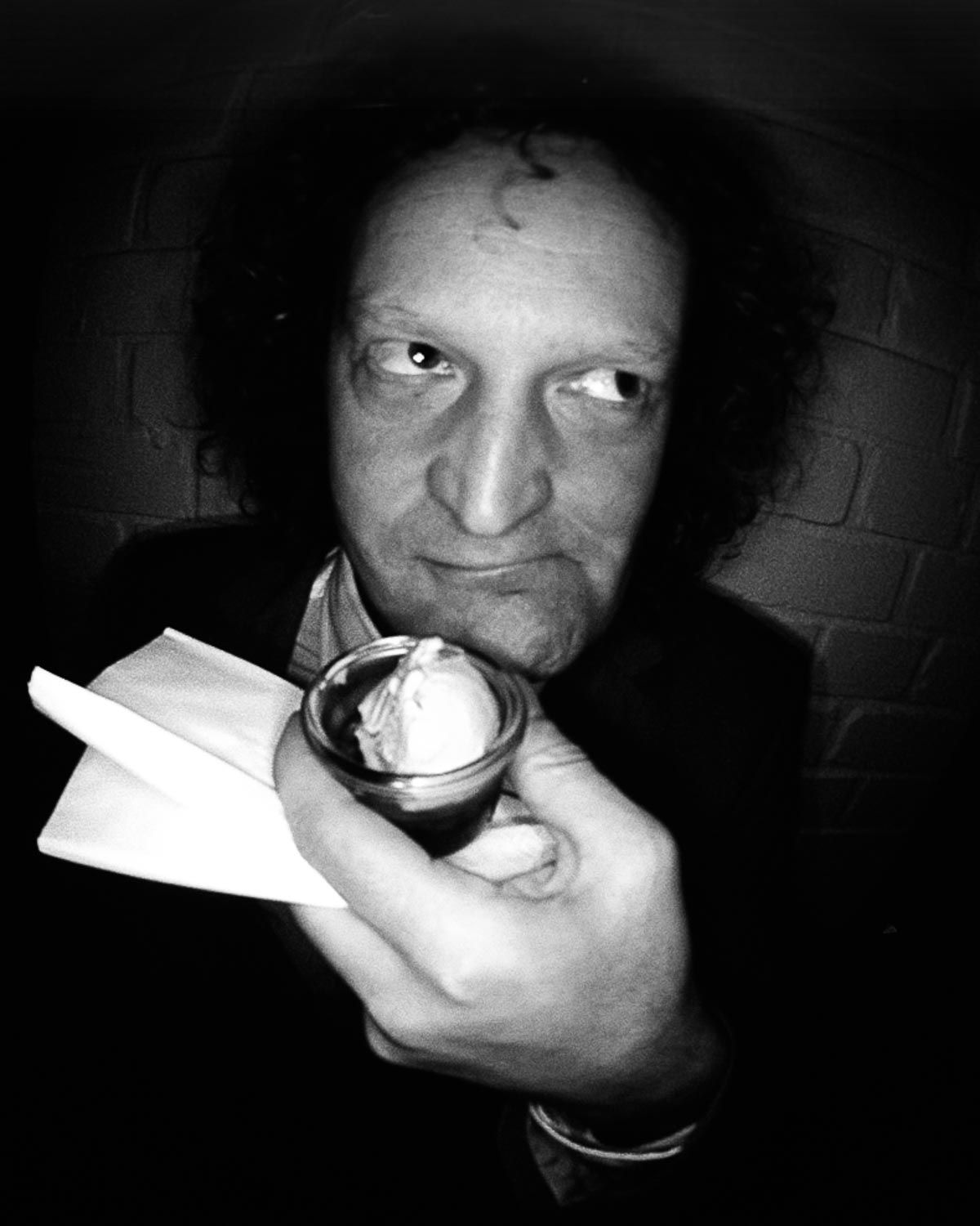 Dramatic black and white portrait of person holding illuminated object in dark setting.