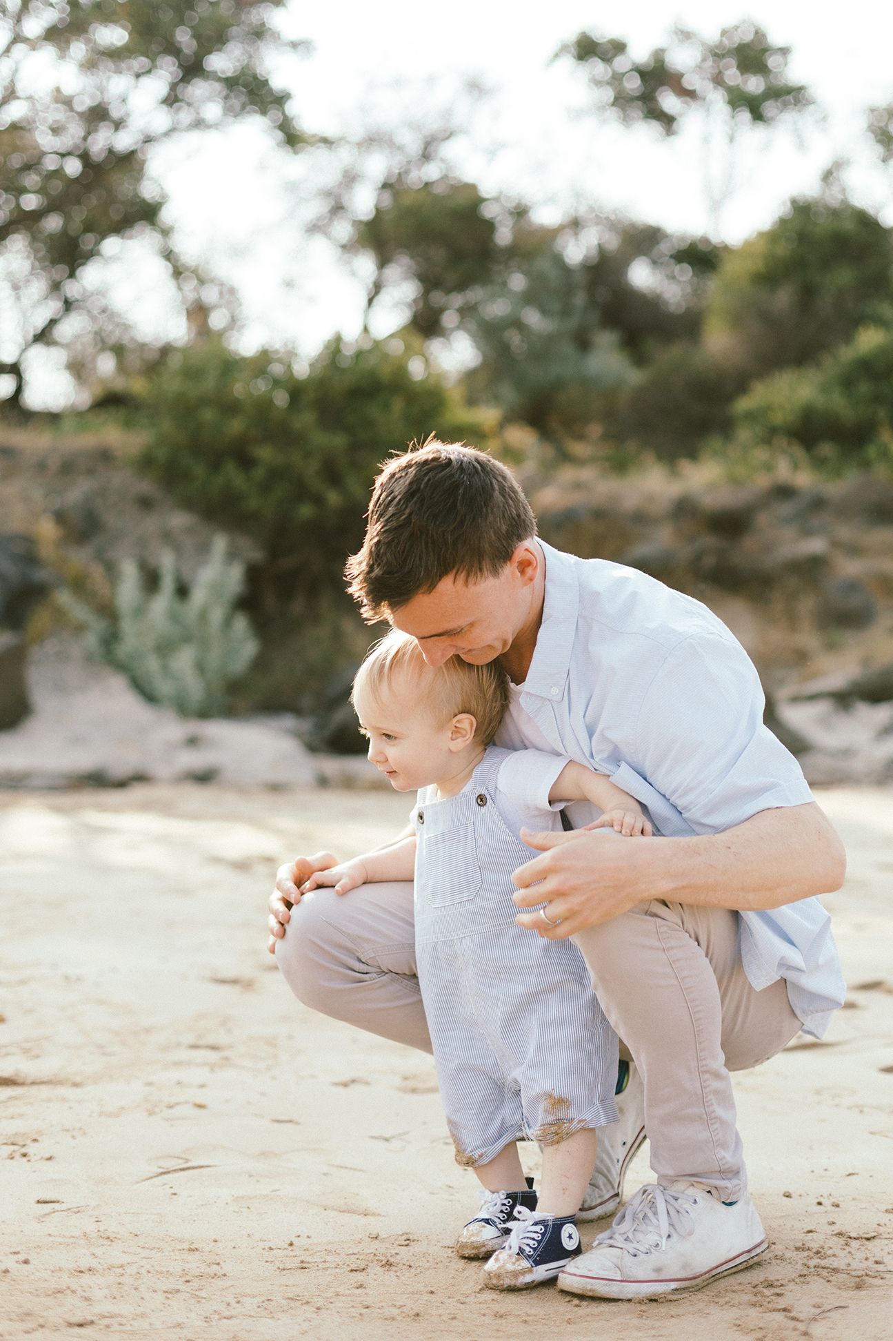 A parent and child play together on sandy ground near desert vegetation.