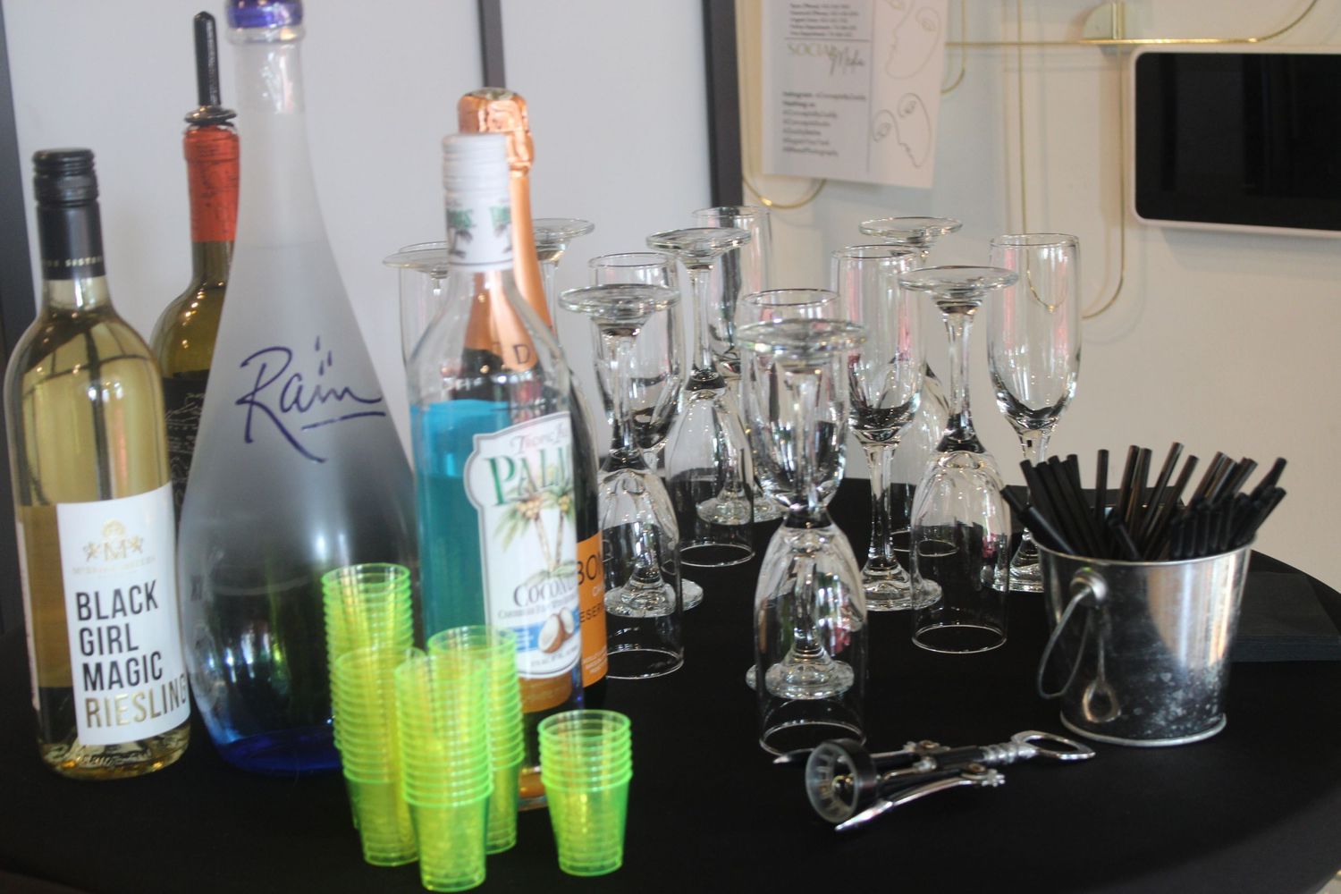 Bar setup with wine bottles, cocktail glasses, and neon green drinks on black surface.