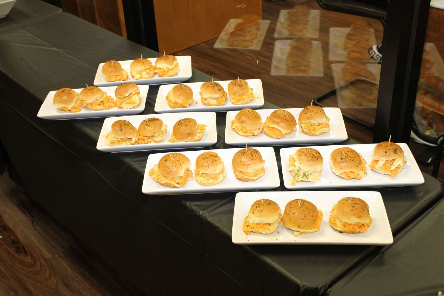 Multiple white plates of golden mini sliders arranged in rows on a dark surface.