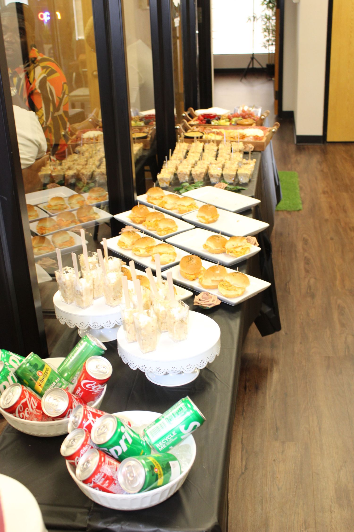 Catering display with mini sandwiches, drinks, and snacks on tiered platters.