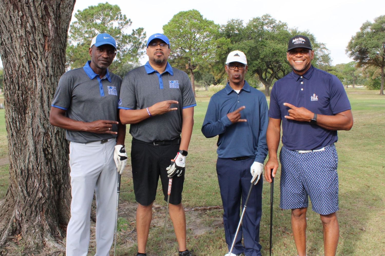 Four golfers pose together on a golf course by a large tree.