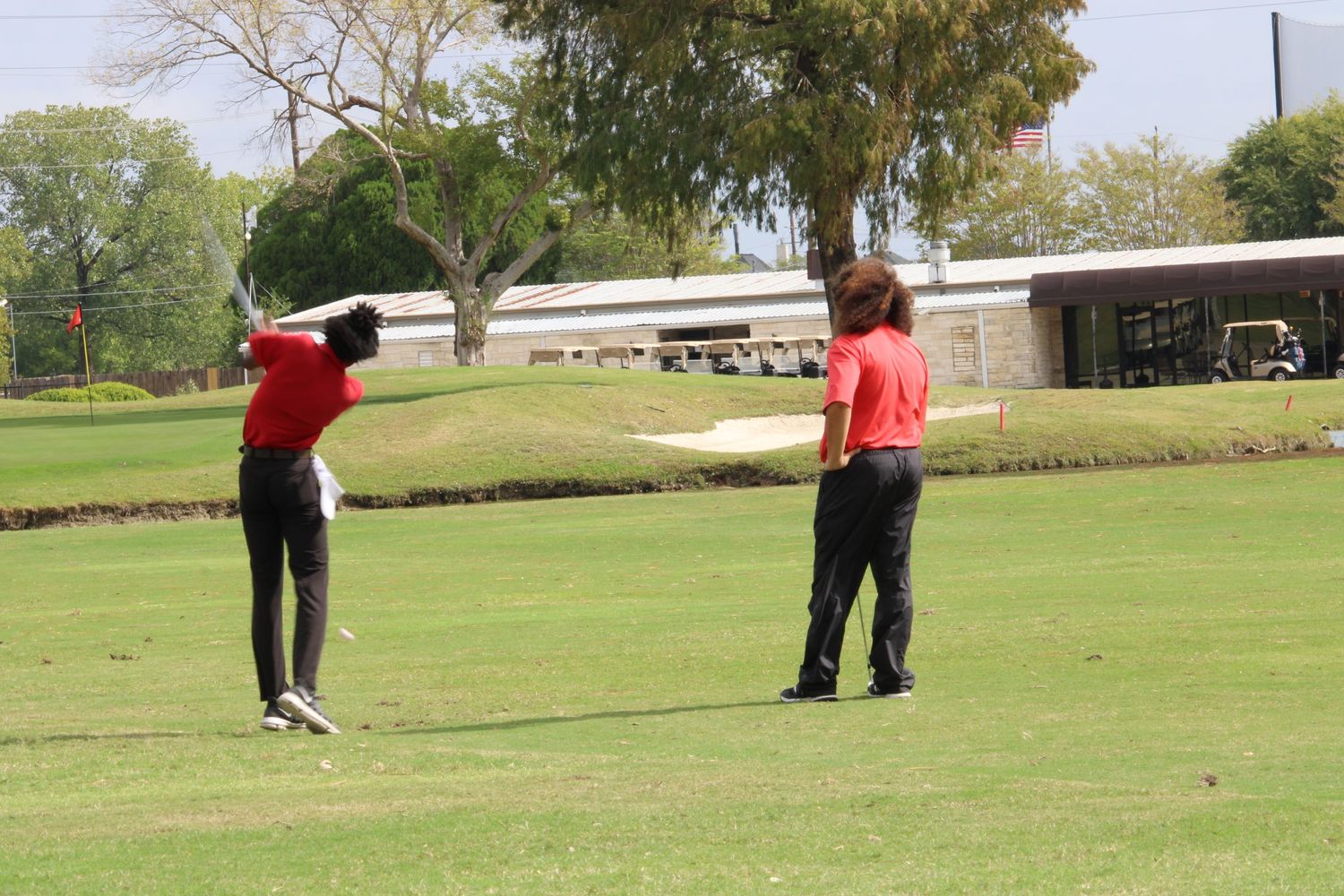 Two golfers in red shirts practicing their swings on a green golf course.