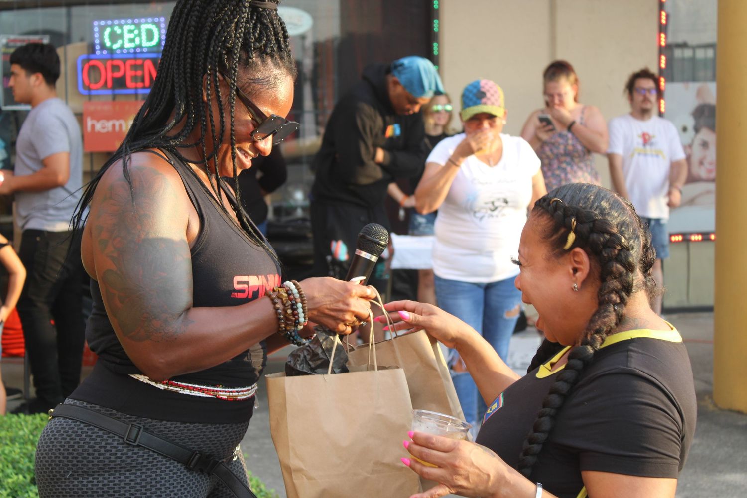 Two people exchanging items from a paper bag at an outdoor community event.