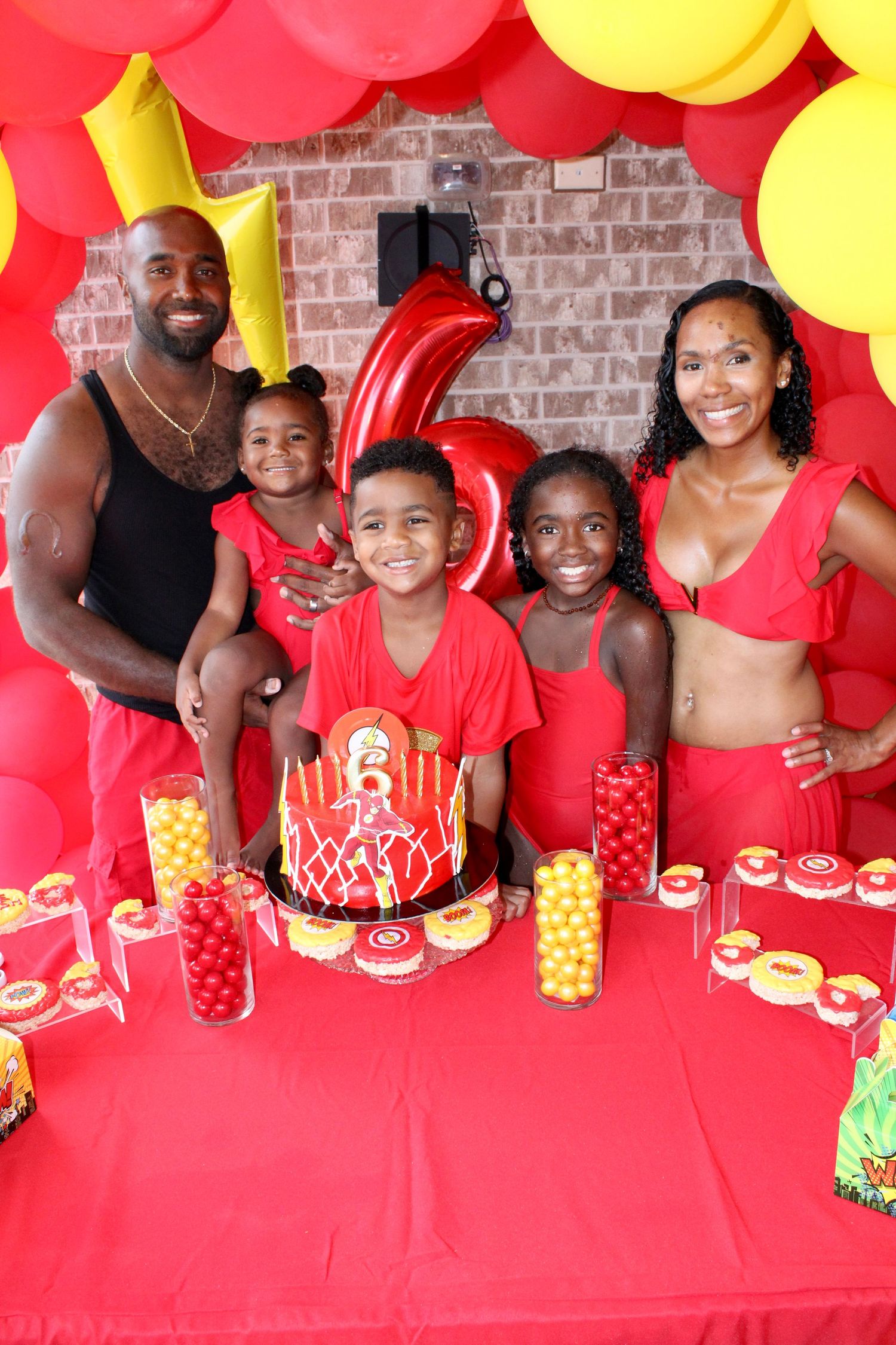 A festive birthday party setup with red and yellow balloons against a brick wall backdrop.