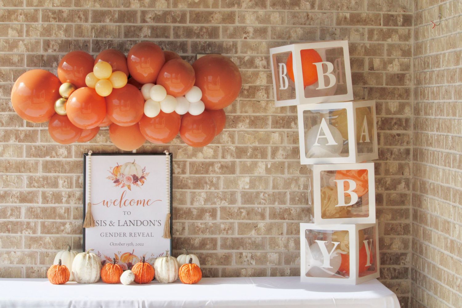 Orange and white balloon arch with baby blocks and pumpkins creating a festive autumn-themed display.
