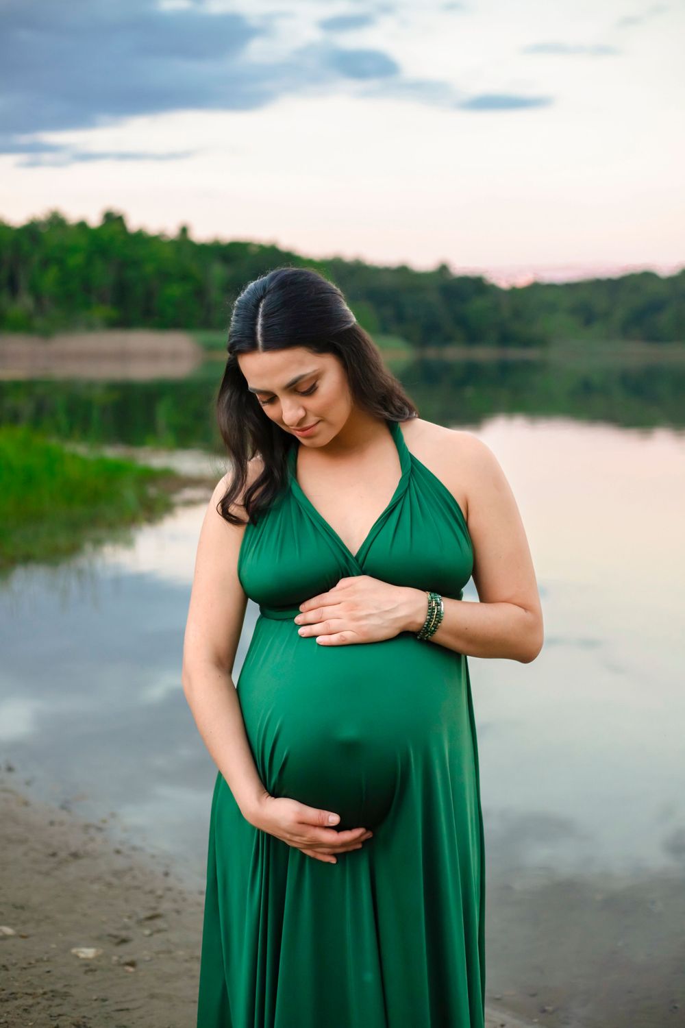 A peaceful maternity moment captured by a lake in a flowing green dress.