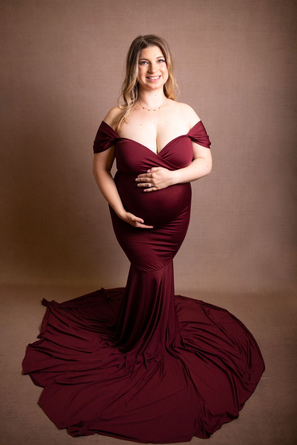 A maternity portrait in an elegant burgundy off-shoulder gown with a dramatic flowing train.