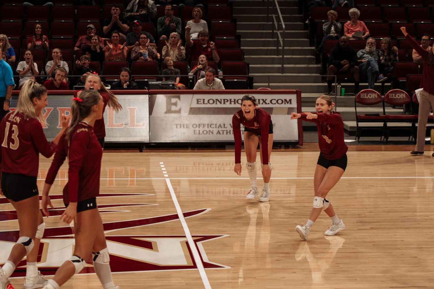Volleyball players warming up before match on indoor court with crowd in background.