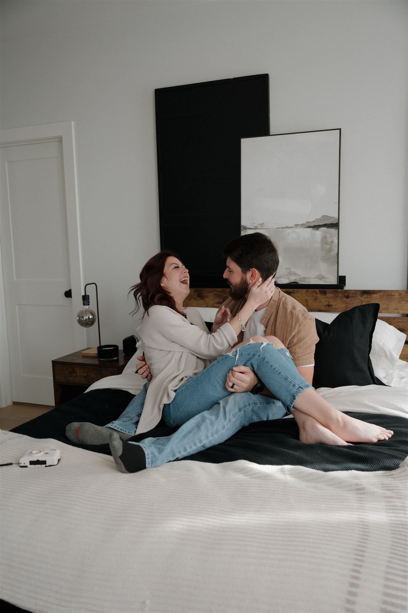 A couple sharing laughter while relaxing on their bed with modern decor in the background.