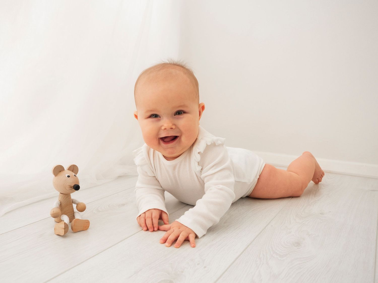 A 7 month old baby lays on her tummy, pushing herself up on her hands and smiling at the camera.