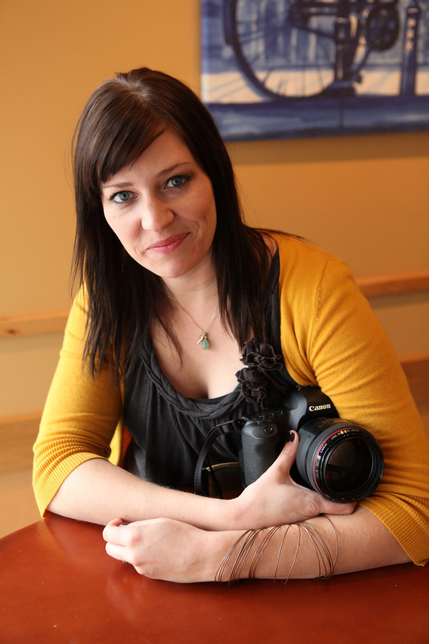 Photographer with camera wearing yellow cardigan and black top resting on wooden table.