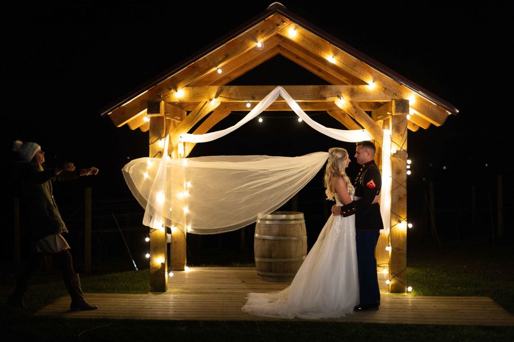 Romantic nighttime wedding scene under illuminated wooden gazebo with flowing fabric.