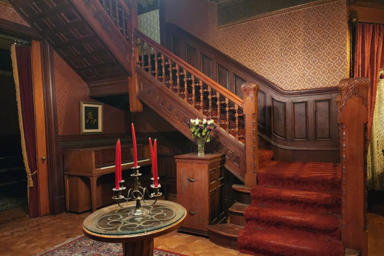 Vintage wooden staircase with red candles and dark wood paneling in gothic interior.