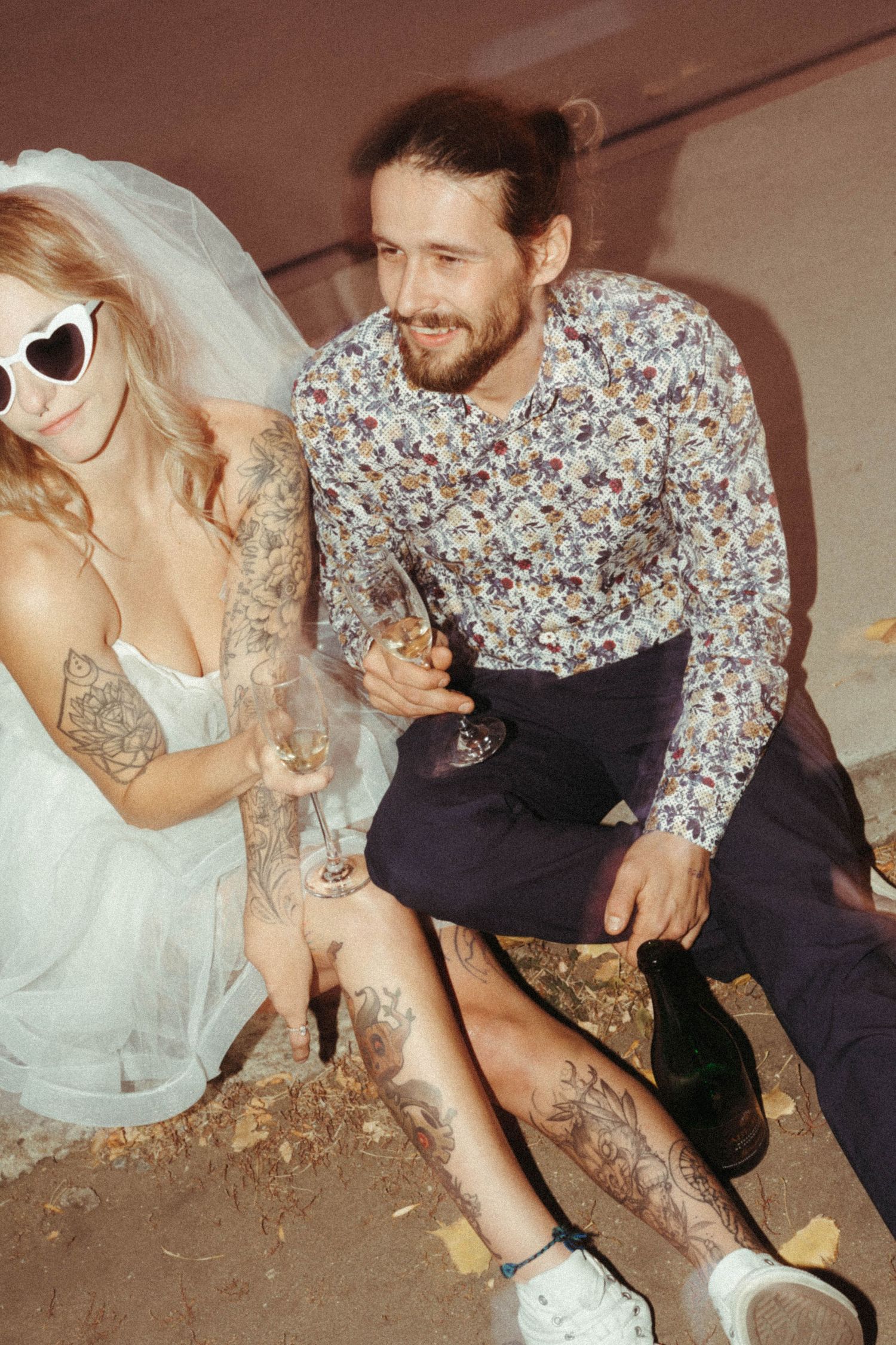 Casual wedding couple in sunglasses and floral print sitting together outdoors.