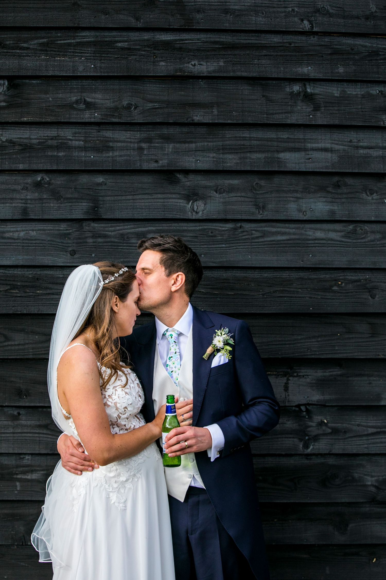 Couple sharing intimate moment against rustic wooden wall during wedding celebration.