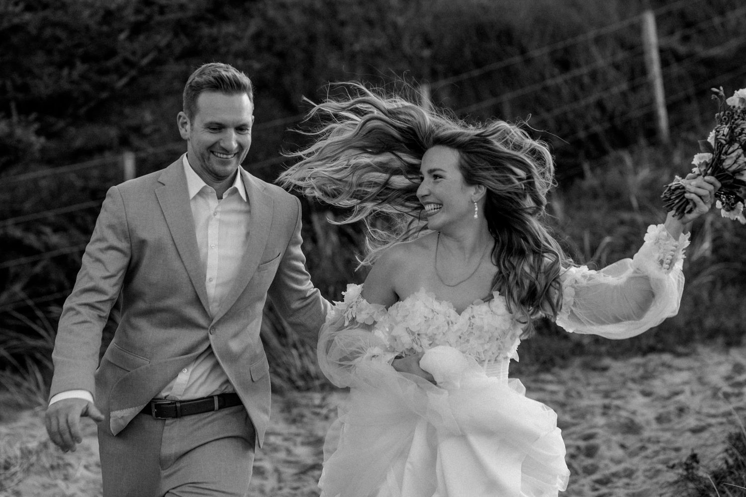 Black and white wedding photo capturing a joyful moment with wind-blown hair.