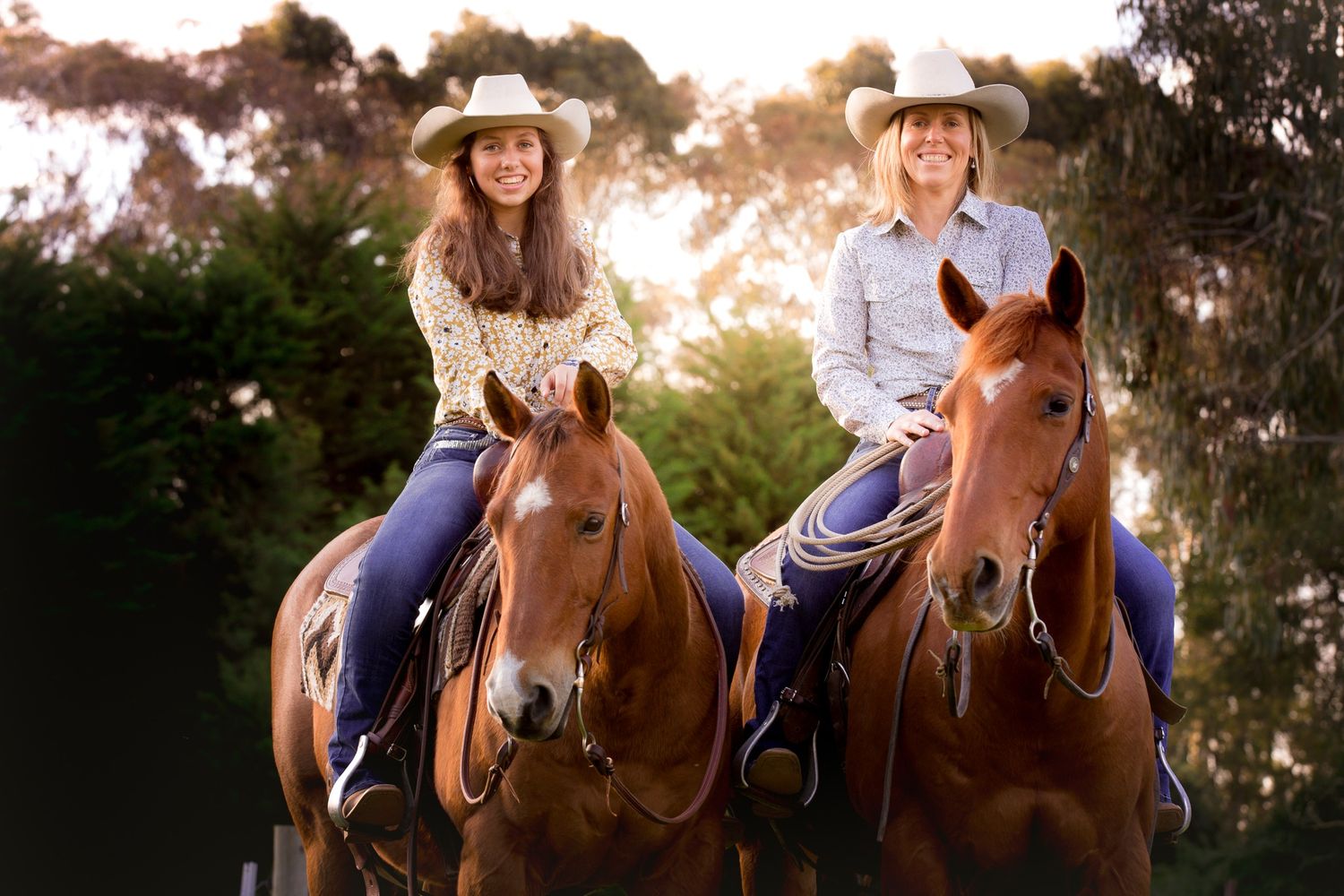 Two riders on horseback enjoying a sunset trail ride through eucalyptus trees.