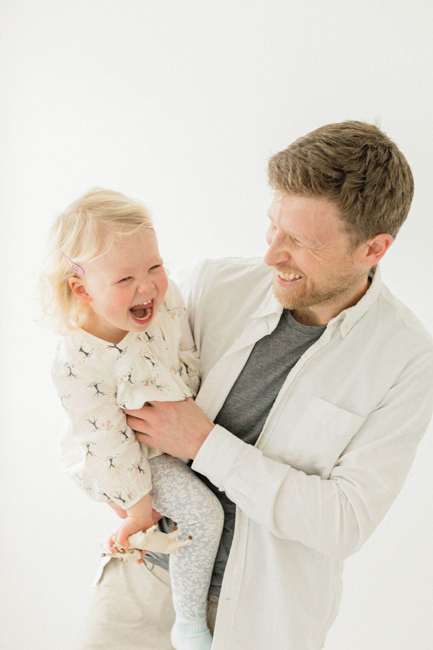 A playful interaction between parent and child wearing white against a light background showing joyful expressions.