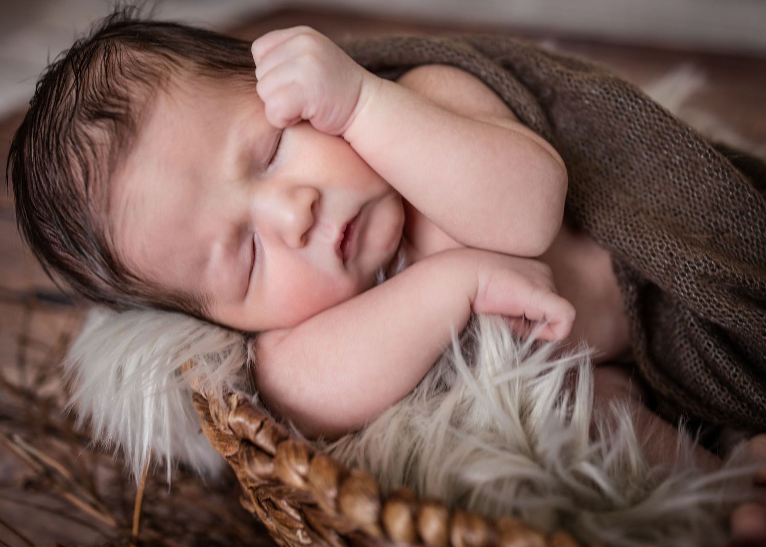 Sleeping infant wrapped in brown blanket lying on soft furry surface in studio setting.