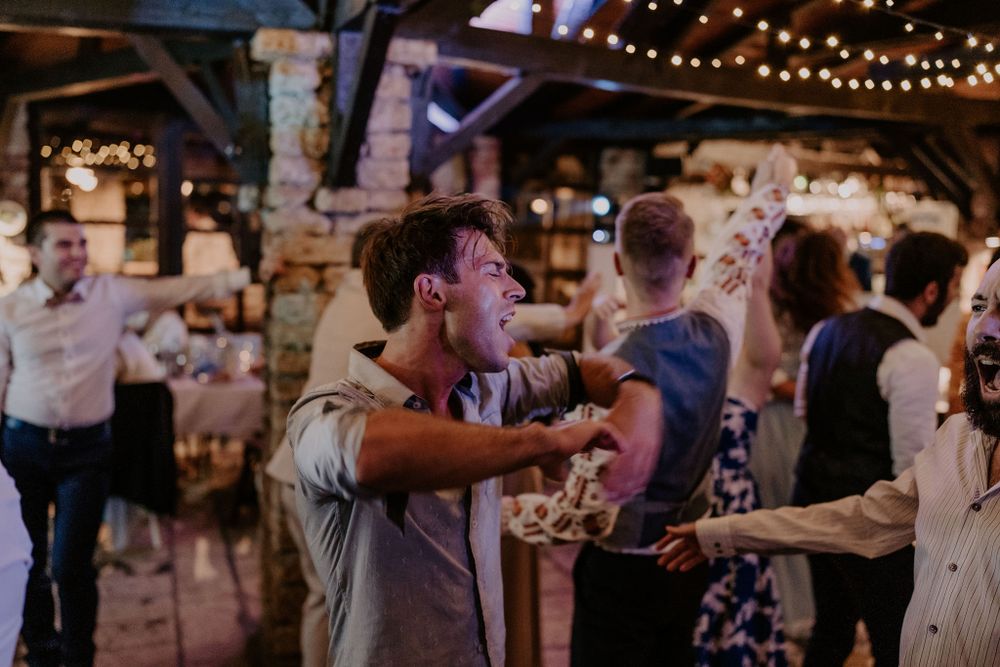 Energetic party guests dancing and moving to music under string lights at a rustic venue.