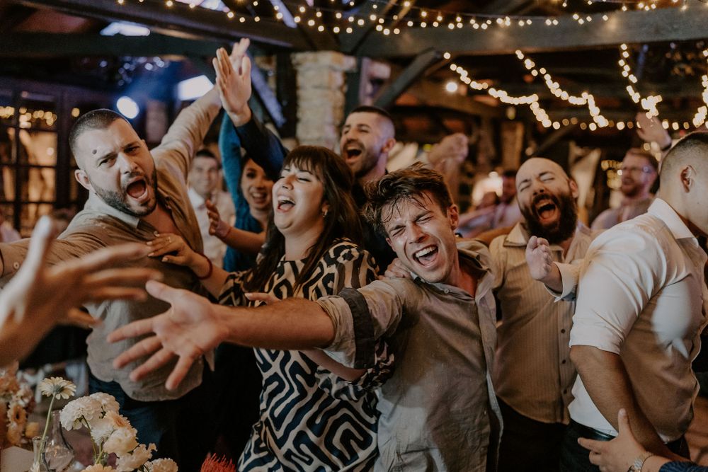 Enthusiastic crowd celebrating with arms raised during a lively wedding reception.