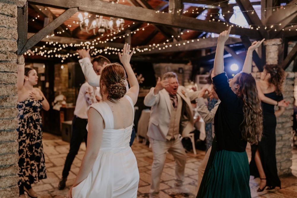 Wedding celebration with guests dancing under twinkling lights in a rustic barn setting.