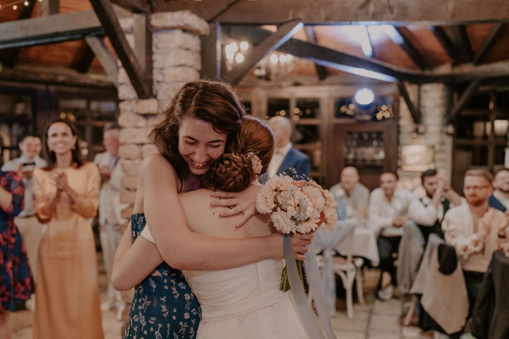 Wedding reception guests embrace and celebrate in a rustic brick-walled venue with twinkling string lights.