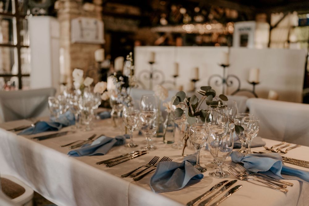 Wedding table setup with blue napkins and crystal glassware in industrial-style venue.