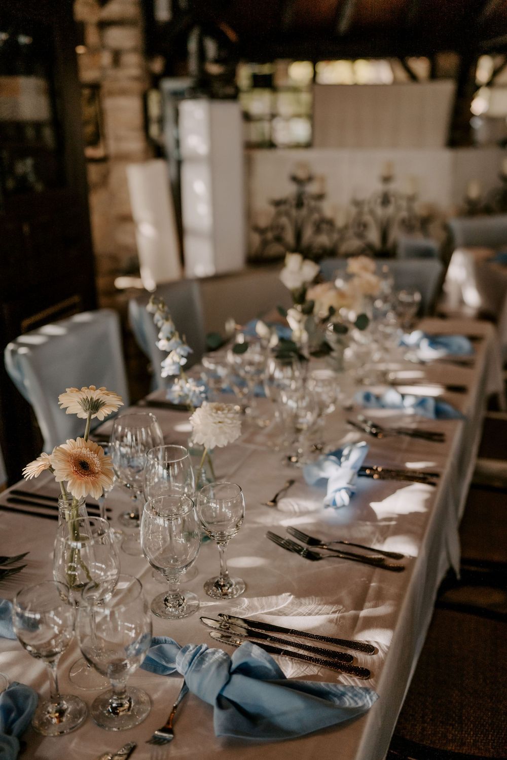 Romantic table setting with pale flowers and blue napkins in rustic indoor space.