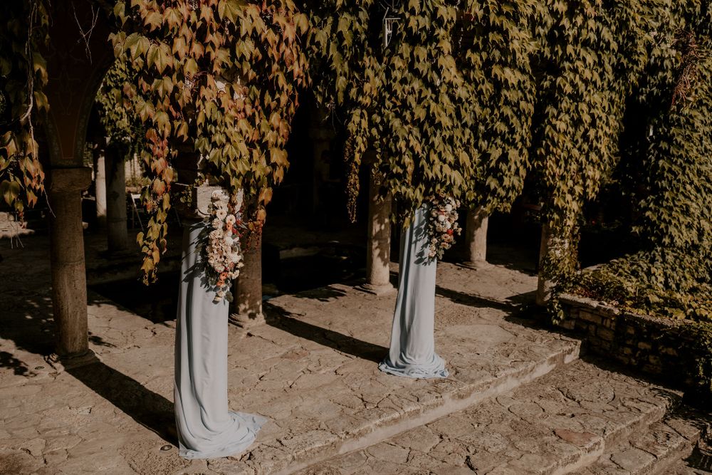 Autumn wedding ceremony setup with white chairs and draped fabric under trees with golden leaves.
