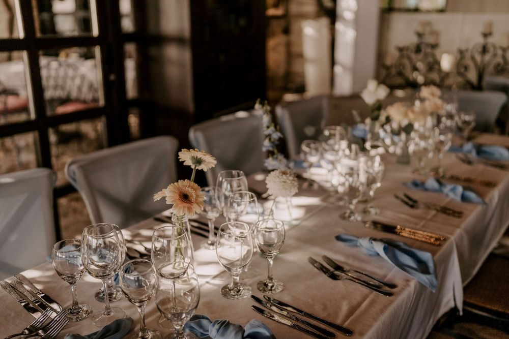 Moody wedding reception table with crystal glasses and floral arrangements in natural light.