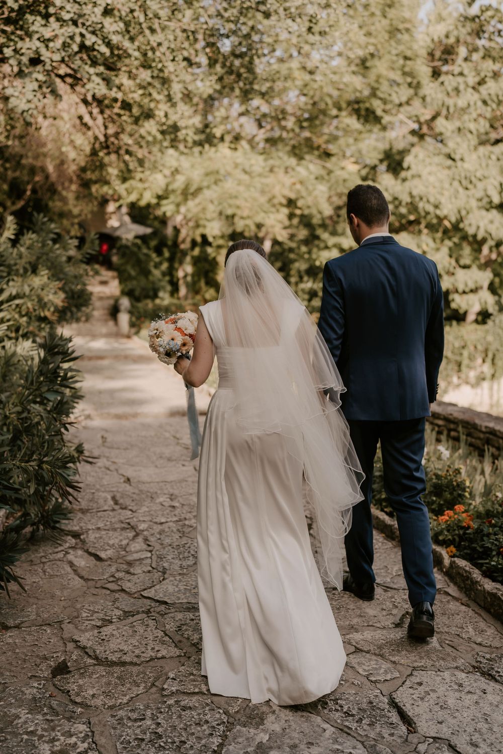 Couple walking along stone garden path surrounded by lush greenery.