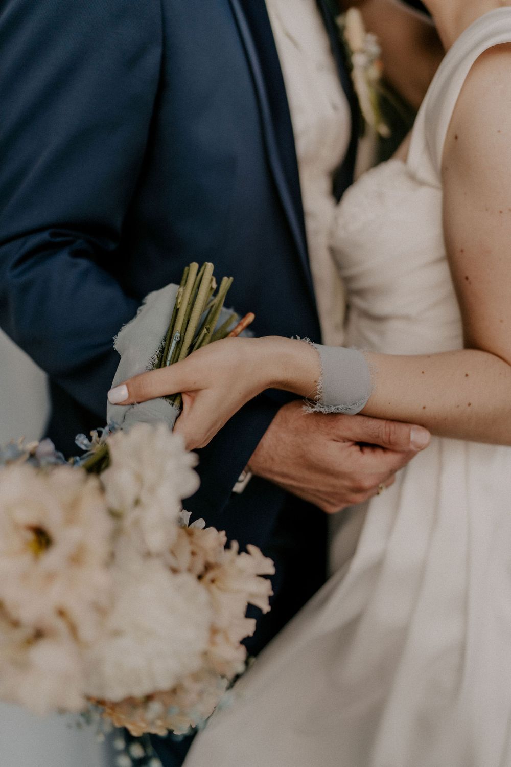 Close-up of wedding couple's hands exchanging rings with white floral bouquet.