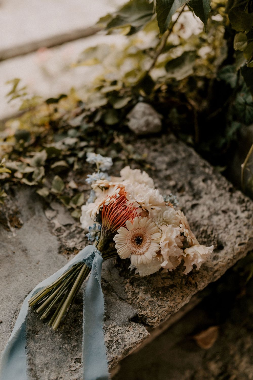 Delicate cream-colored wedding bouquets with soft ribbons resting on stone.