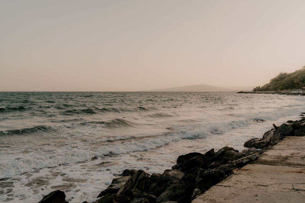 Tranquil ocean waves crash against rocky shore during sunset with misty atmosphere.