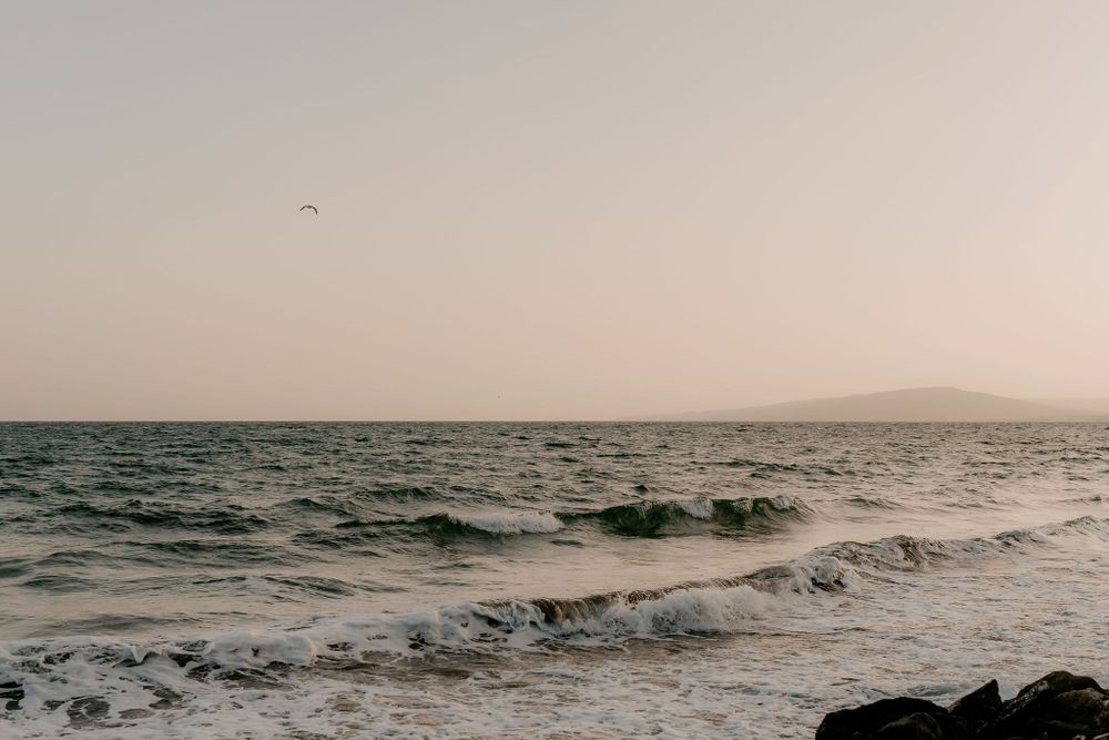 Dramatic seascape with waves rolling against dark rocks at dusk.