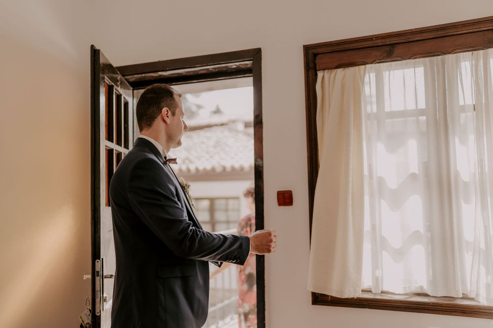 Two people in formal attire prepare for a special occasion in a sunlit room.