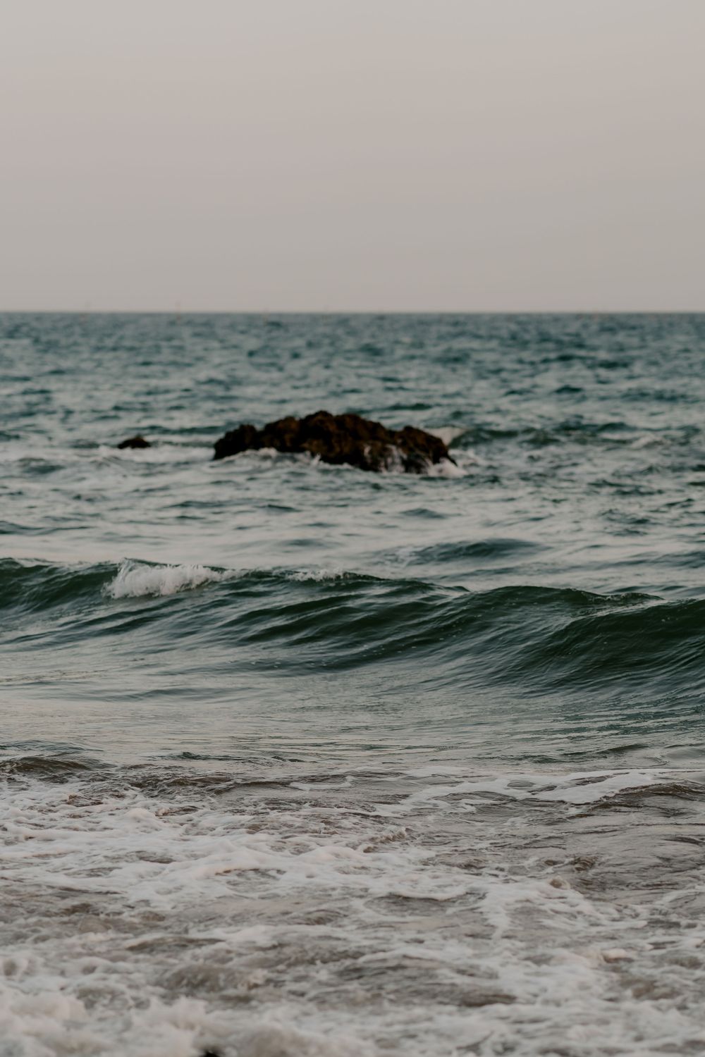 Rolling waves meet rocky coastline under overcast sky at dusk.
