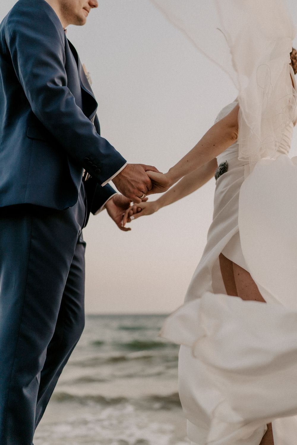 Elegant couple in formal attire dancing by the ocean at sunset.