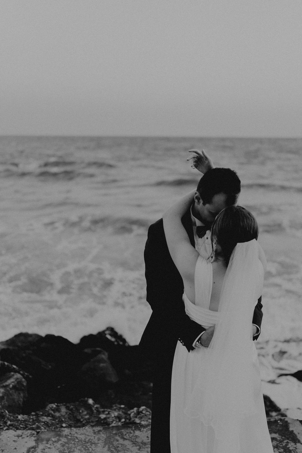 Black and white wedding photo capturing an intimate moment between newlyweds by the ocean.