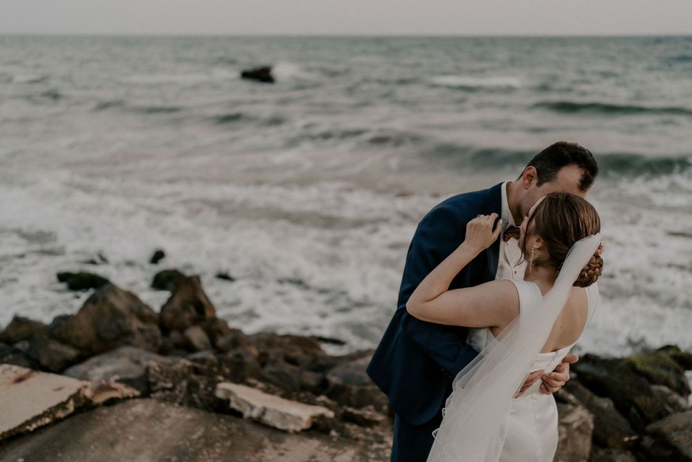 Newlyweds share tender moments along a dramatic coastline with crashing waves.