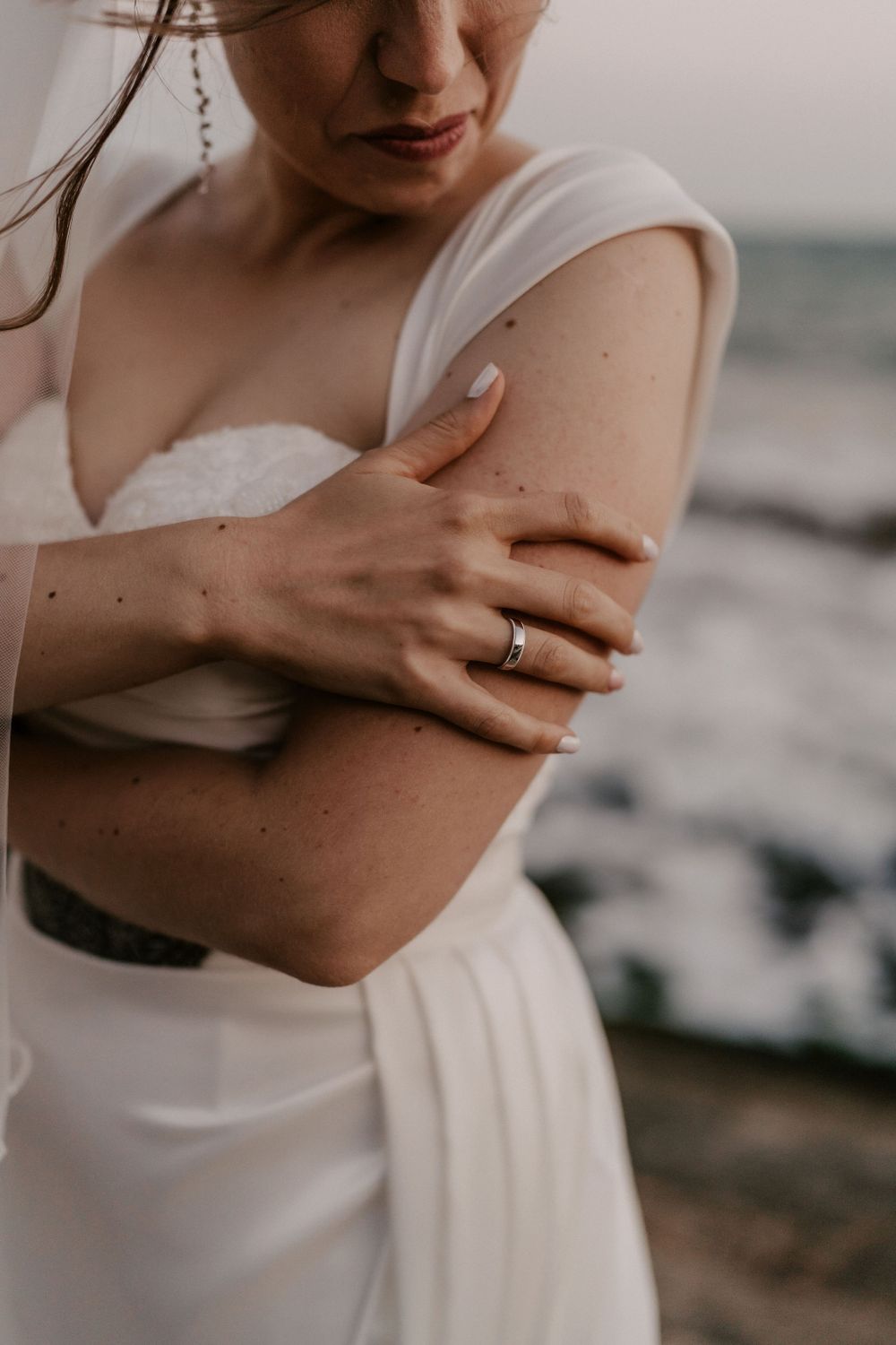 Close-up details of a bride's elegant white wedding dress and delicate hands.
