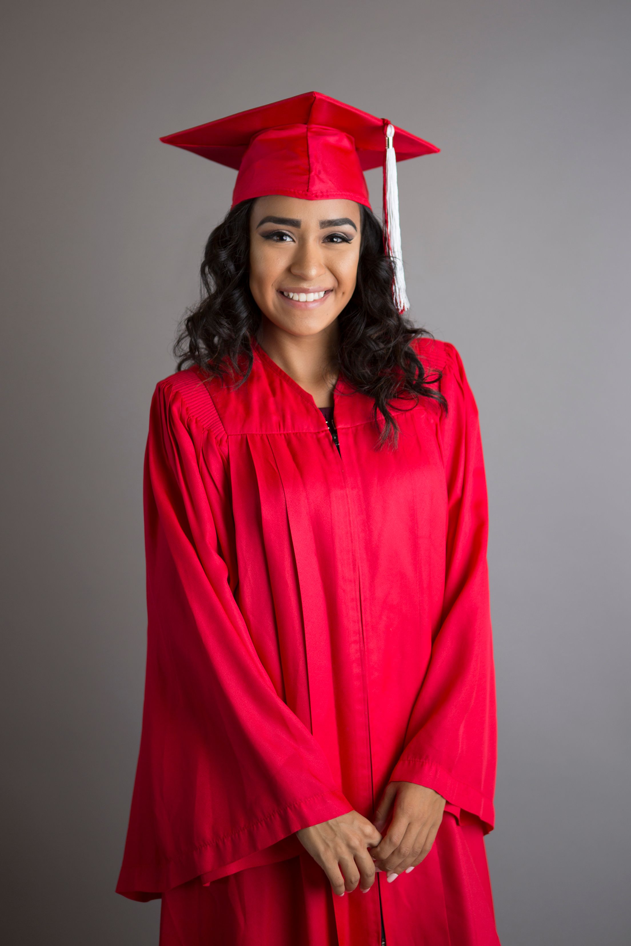 Graduate in bright red cap and gown smiling during graduation photo session.